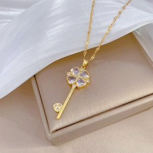 Close-up of a gold key necklace with clover-shaped clear gemstones on white silk