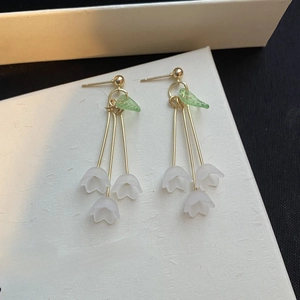 Detail of white frosted lily of the valley earrings with gold fringe and green leaf accents