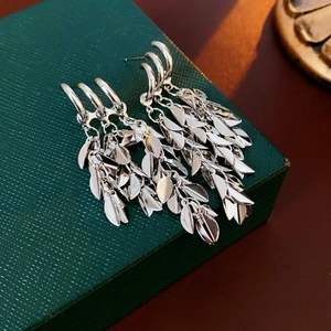 Detailed view of silver wheat ear tassel earrings on a textured green jewelry box