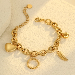 Detalle de pulsera dorada vintage con dijes de corazón y cuerno sobre fondo de piedra natural