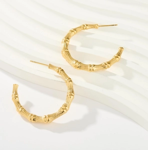 Close-up of 18K gold C-shaped earrings with vintage bamboo texture on white wave base
