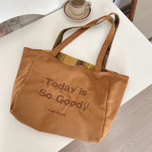 Close-up of brown suede tote bag featuring embroidered text and yellow plaid lining