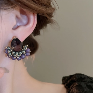 Close-up of purple teardrop zircon earrings with bead trim worn on the ear