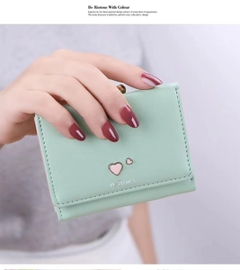 Close-up of mint green tri-fold wallet featuring a pink heart charm held by a model