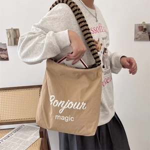 Detail of khaki tote bag with Bonjour print and striped plush shoulder strap on a model