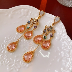 Detailed close-up of gold dangle earrings with pink teardrop crystal and rainbow rhinestones