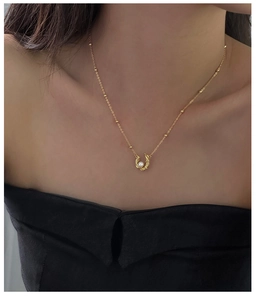 Detail of horseshoe pearl pendant on golden bead chain worn on model's neck