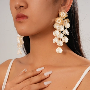 Elegant gold tassel earrings with white shell flowers worn by a model on a clean background