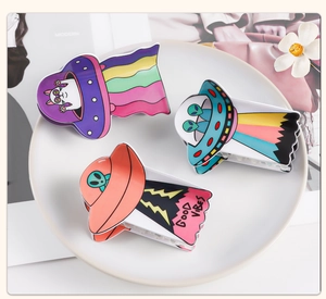 Close-up of three colorful UFO cartoon hair claws with alien designs on white ceramic tray