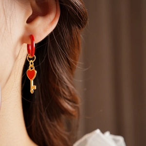 Detail of a gold key earring with a red enamel heart drop and small red ring accent