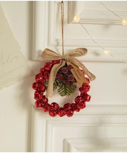 Red metal Christmas bell wreath with burlap bow and pine needles hanging on a wall