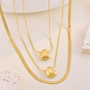 Detail of layered gold necklaces featuring a polished heart pendant and a flat snake chain