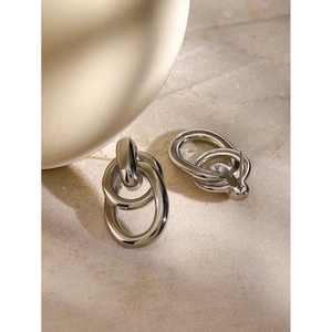 Macro shot of silver intertwined geometric earrings on light stone texture surface
