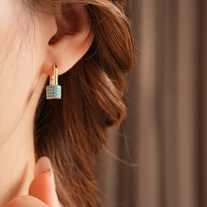 Detail of gold huggie earring with turquoise cylindrical charm worn by a model