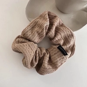 Macro detail of beige knitted scrunchie showing cable stitch texture and material label