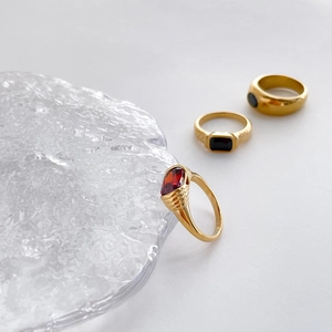 Detail of gold rings with red and black gemstones on a textured glass pedestal