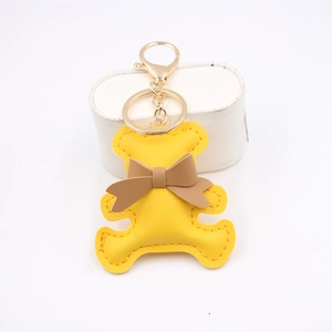 Cute yellow leather bear keychain with brown bow and gold metal ring on white background