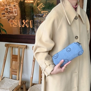 Macro detail of sky blue corduroy makeup bag with embroidered smiley faces and zipper