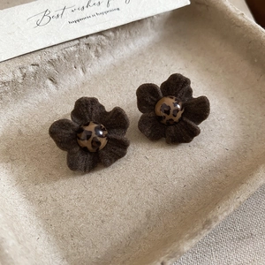 Macro shot of brown velvet flower earrings with leopard print beads on a beige tray