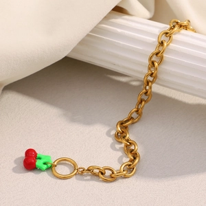 Macro detail of gold-plated thick link bracelet featuring a red enamel cherry charm