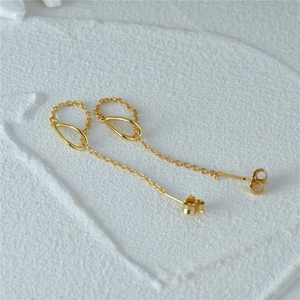 Macro shot of gold teardrop earrings with elegant chain tassels on textured white background