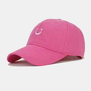 Detail view of pink baseball cap featuring white embroidered smiley face and cotton texture