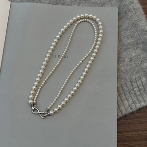 Detail of double-layer pearl necklace with infinity symbol clasp on grey fabric background