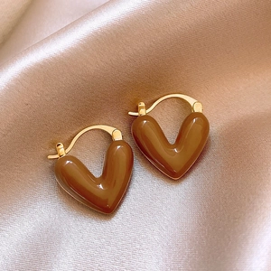 Macro detail of heart shaped brown tiger eye earrings on premium champagne silk fabric