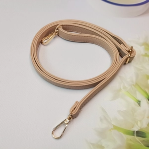 Detalle de correa de bolso ajustable beige motivo litchi con mosquetones y hebilla oro