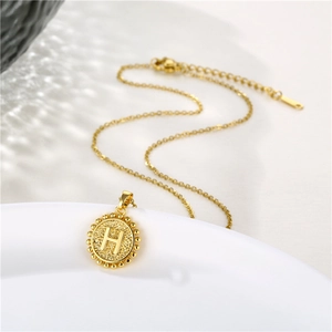 Detail shot of golden necklace featuring a vintage round pendant with letter H engraving