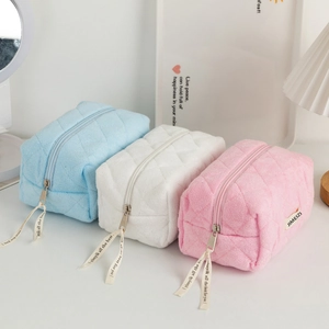 Close-up of three quilted plush cosmetic bags in blue, white, and pink with ribbon zippers
