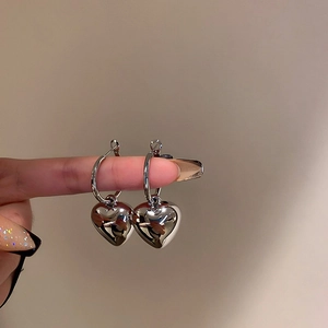 Detail of silver heart charm hoop earrings held by hand, showing high-gloss metallic finish