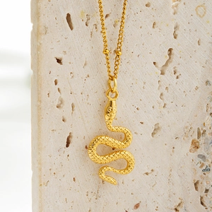 Close-up of golden snake pendant with textured scales on a thin chain over beige stone