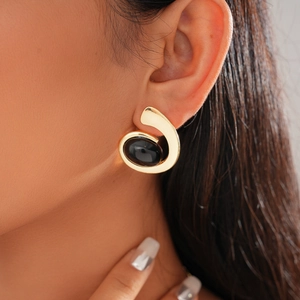 Detailed close-up of a gold metal geometric earring with oval black resin inlay on model