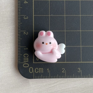 Pink resin rabbit with white wings charm accessory shown on a measurement cutting mat