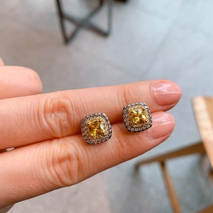 Detail of square yellow zircon earrings with silver halos held between two fingers