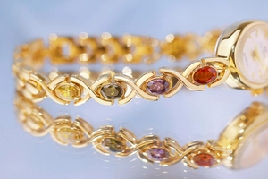 Close-up of gold bracelet watch featuring multi-color oval gemstones with clear reflections