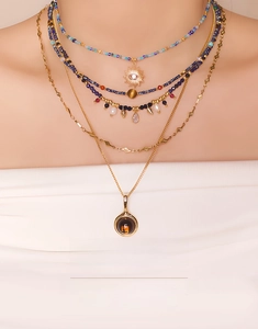 Detail of layered beaded necklace with evil eye and sun charms on a female model