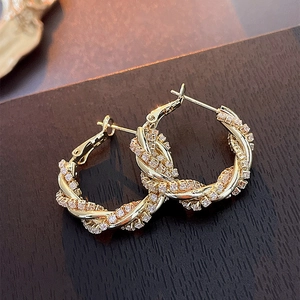 Detailed view of gold twisted hoop earrings with sparkling zircon inlay on wood