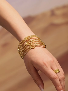 Détail d'un bracelet à perles dorées avec cœurs et bague texturée portés par un mannequin