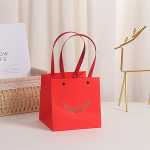 Rote quadratische Geschenktüte aus Papier mit Smiley-Ausschnitt und Seidengriffen