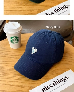 Detail of white heart embroidery on a navy blue cotton baseball cap on a wooden table
