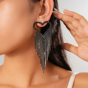 Detail of dark heart-shaped earrings with long black rhinestone tassels on a female model