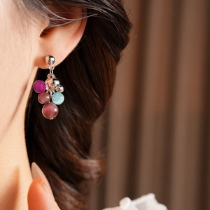 Close-up of cat-eye stone tassel earrings with colorful purple and pink beads on model