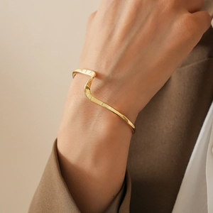 Macro shot of gold twisted wave cuff bracelet showcasing polished irregular geometric curves