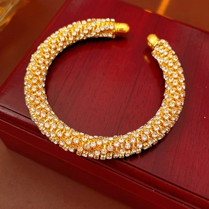 Détail d'un bracelet jonc ouvert doré avec pavé de cristaux sur un écrin à bijoux rouge