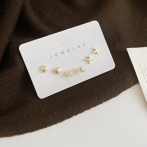 Detailed view of gold minimalist heart, cube, and cross stud earring set on display card