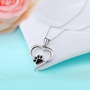 Macro view of silver heart pendant with black paw print detail on a soft blue fabric