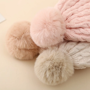 Close-up of cable knit baby beanies with fluffy faux fur pom-poms in pastel colors