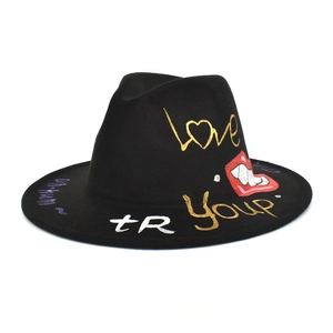 Detail of black fedora hat featuring artistic hand-painted graffiti text and red lip design